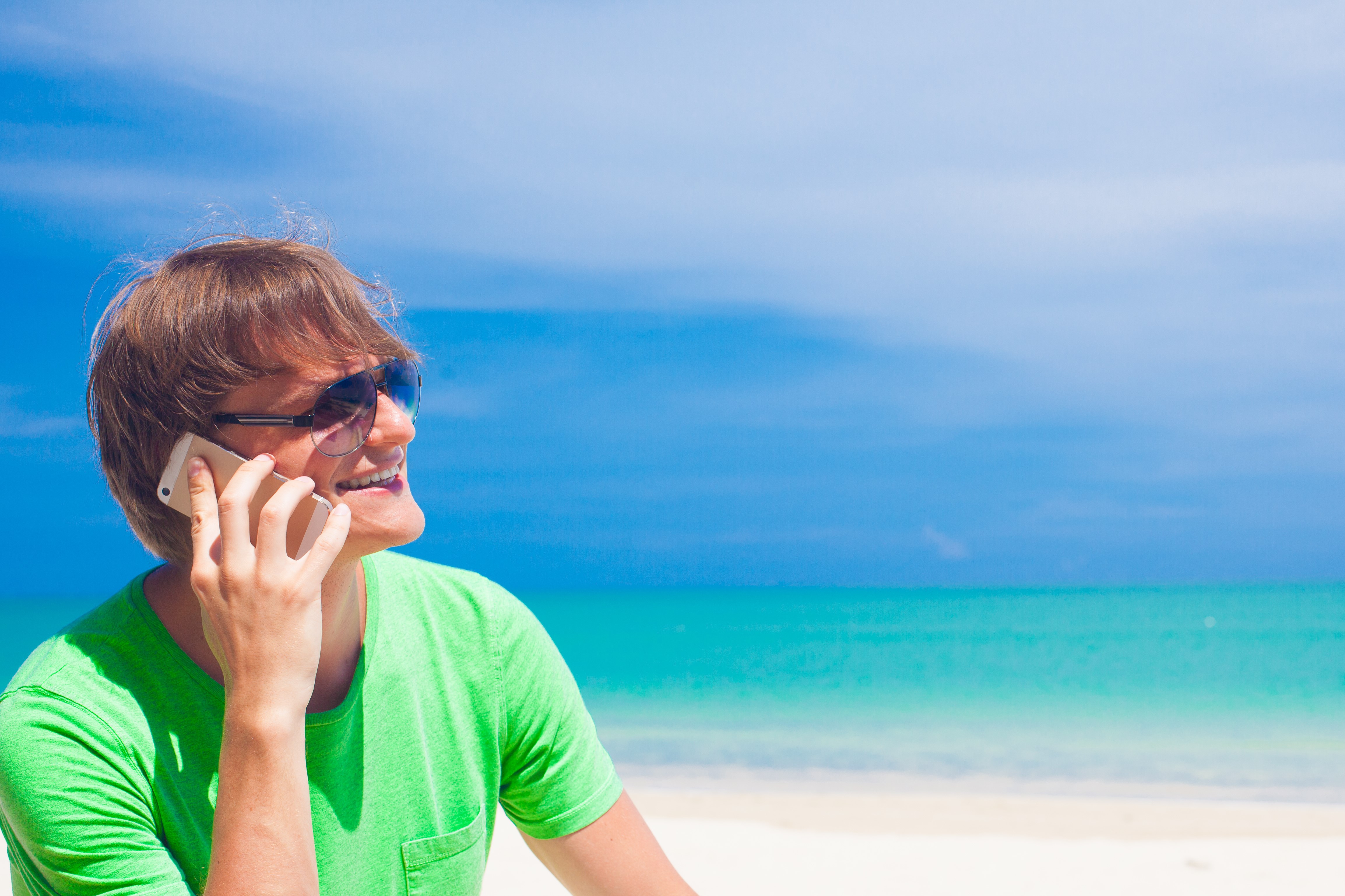 En mann på stranden som snakker i en mobiltelefon. Foto.