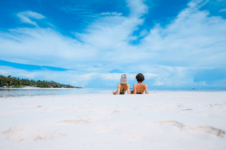 To personer ligger på en strand og ser utover havet. Foto.