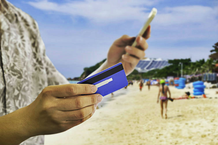 Mann som holder en mobiltelefon og et bankkort mens han er på en strand. Foto.