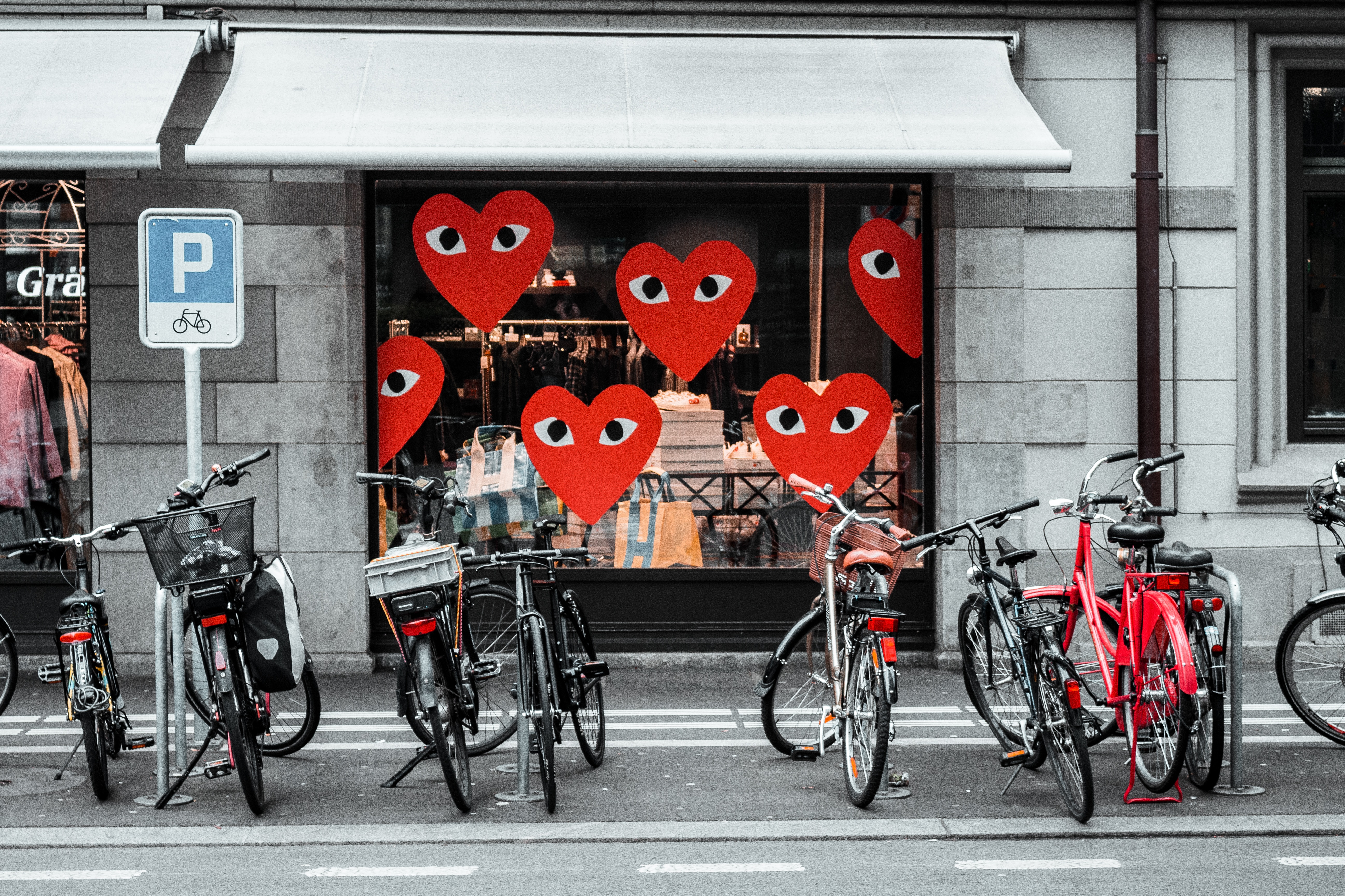 Flere sykler parkert foran en butikk som har røde hjerter i vinduet. Foto.